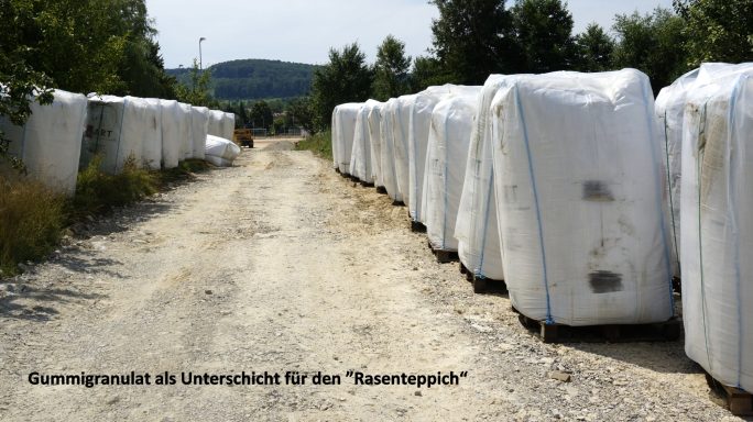 Weiße Kunststoffballen entlang eines schottrigen Weges in einer ländlichen Umgebung.