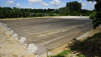 Eine große, ebene Baustelle mit einem klaren blauen Himmel und vereinzelten Wolken.