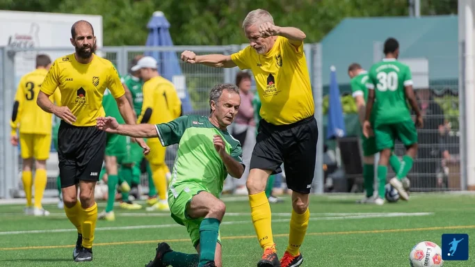Zwei Fußballspieler in gelben Trikots feiern einen Spielzug, während ein Spieler am Boden liegt.