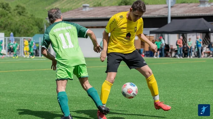 Zwei Fußballspieler im Duell, einer in Gelb, der andere in Grün, auf einem Spielfeld.